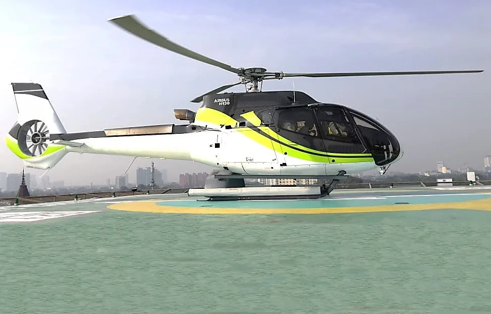 An Airbus H130 helicopter on a helipad with a city skyline in the background.