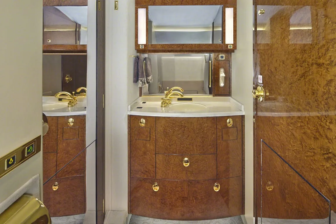 A private jet lavatory with a vanity, sink, and polished wood cabinetry.