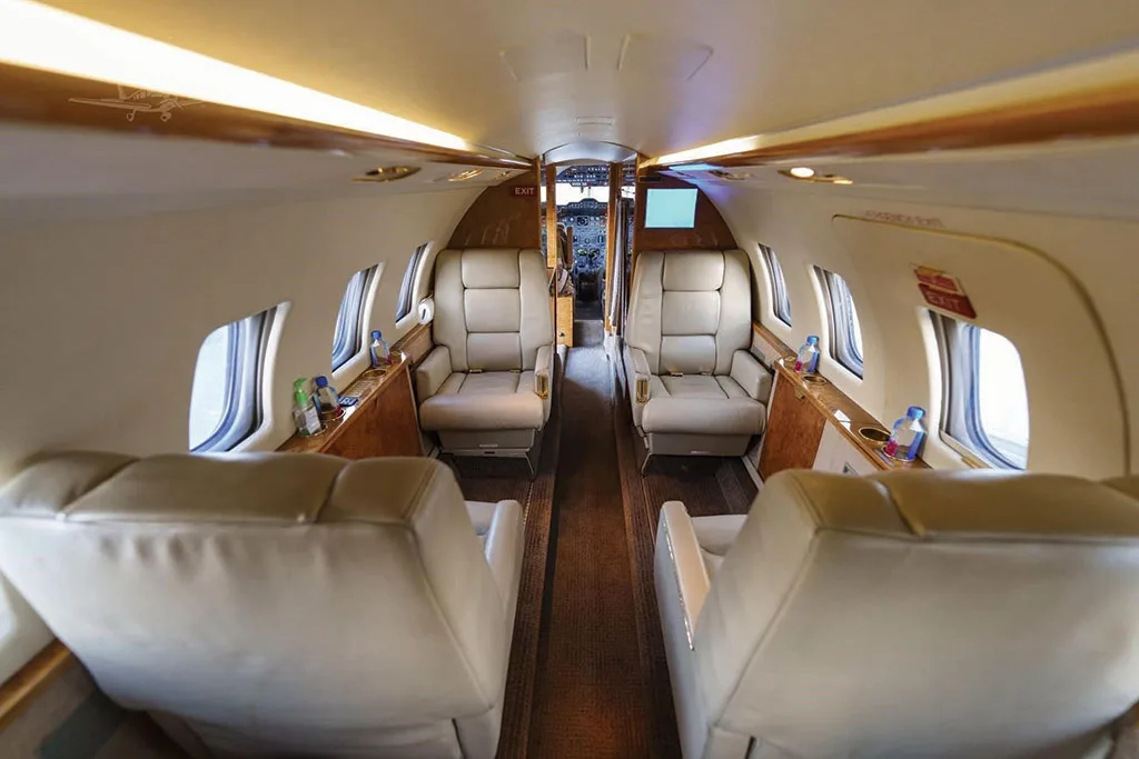A view down the aisle of the Dassault Falcon 50's cabin, showing beige leather seats, wood paneling, and the cockpit entrance in the distance.