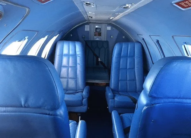 The aircraft cabin features blue leather seats arranged in a club configuration.