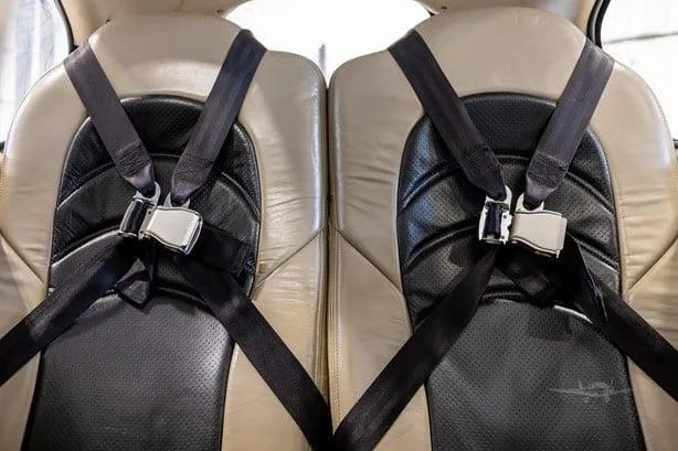 Close-up of two tan leather aircraft seats with black four-point harnesses.