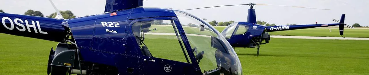 Two blue Robinson R22 Beta helicopters on a grassy field.