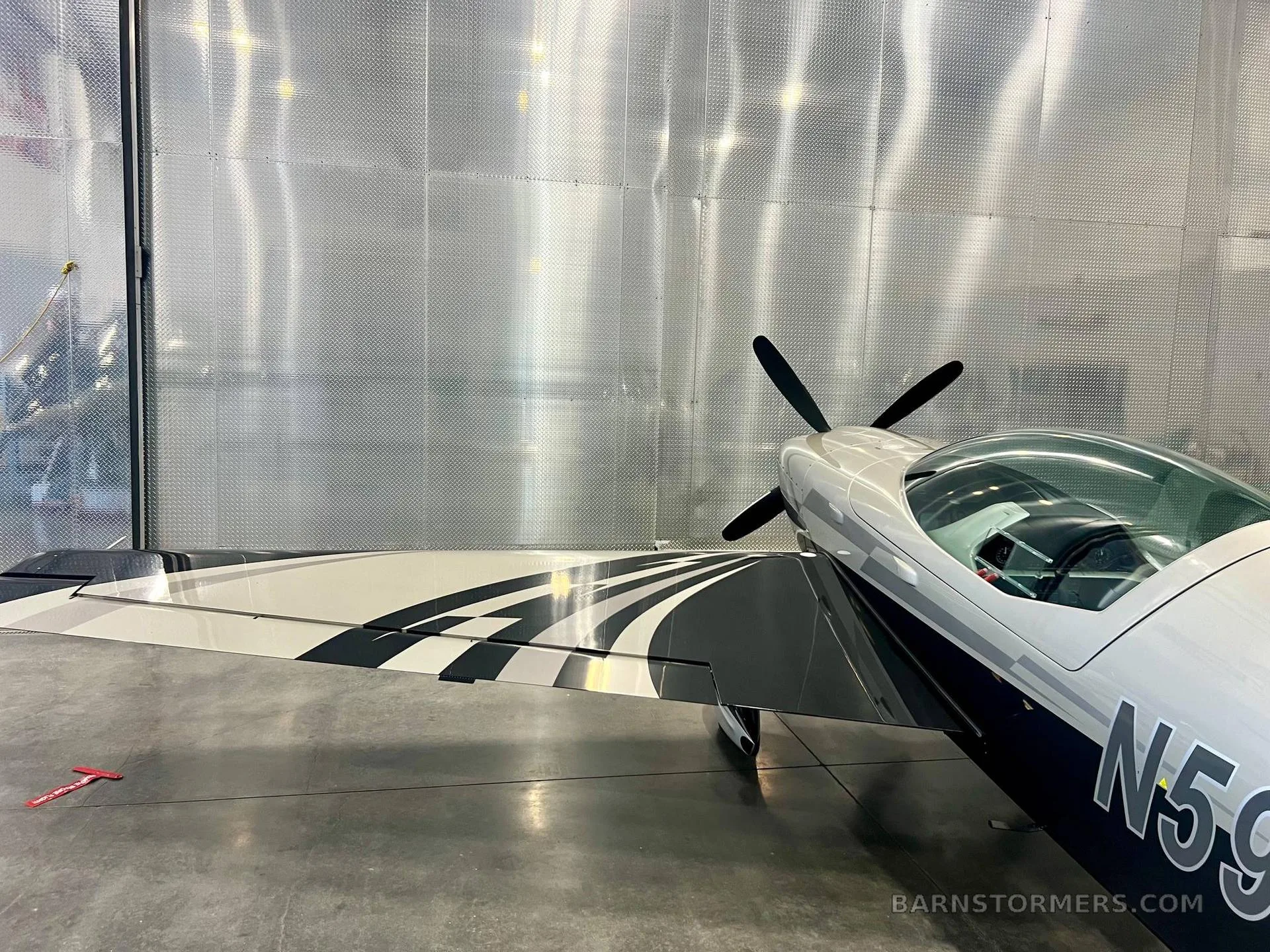 A close-up view of the wing and front fuselage of the silver and black propeller aircraft, N595MK, showing its paint scheme.