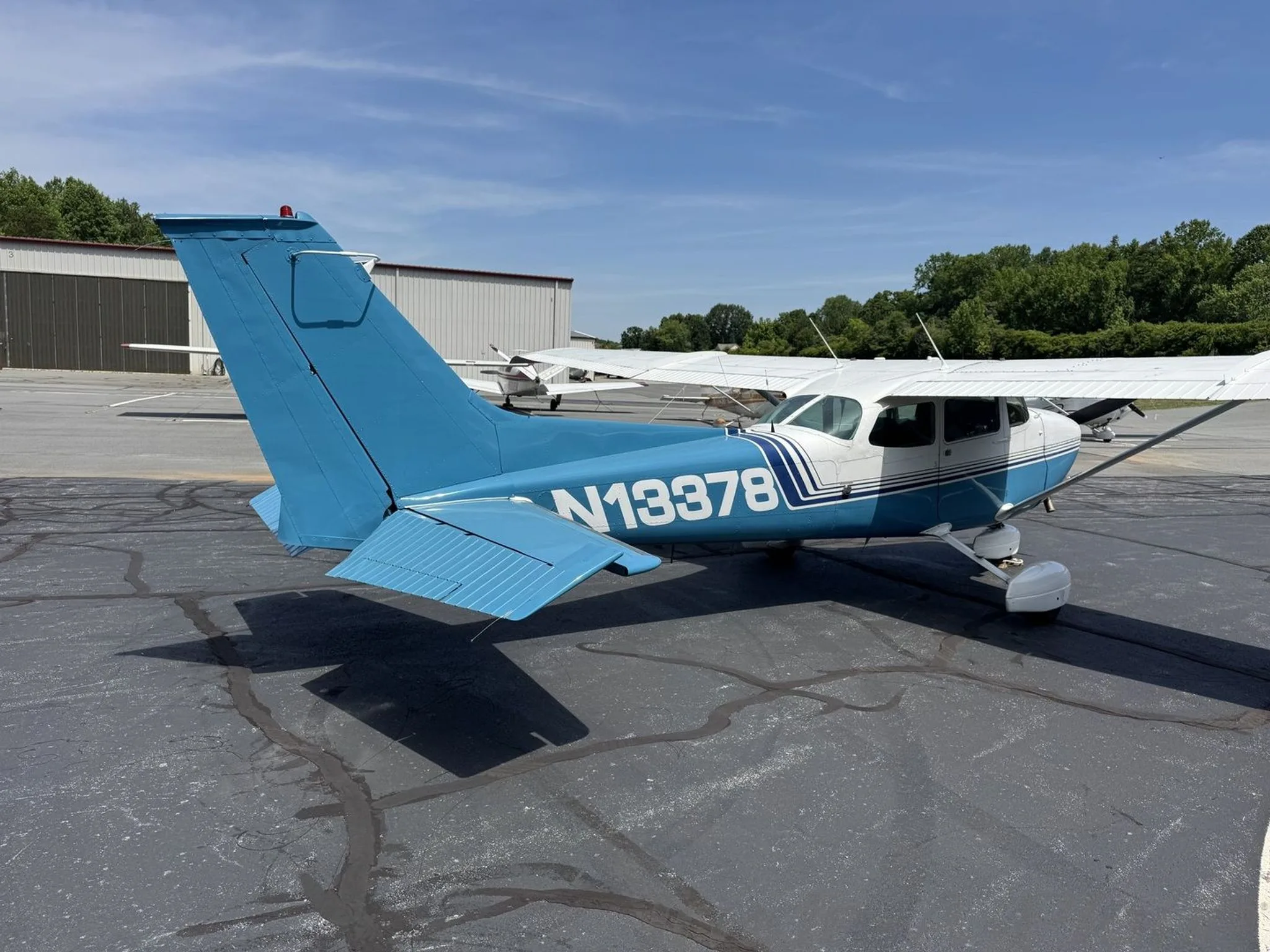 A rear-right view of the blue and white Cessna 172 Skyhawk (N13378) parked on an asphalt apron.