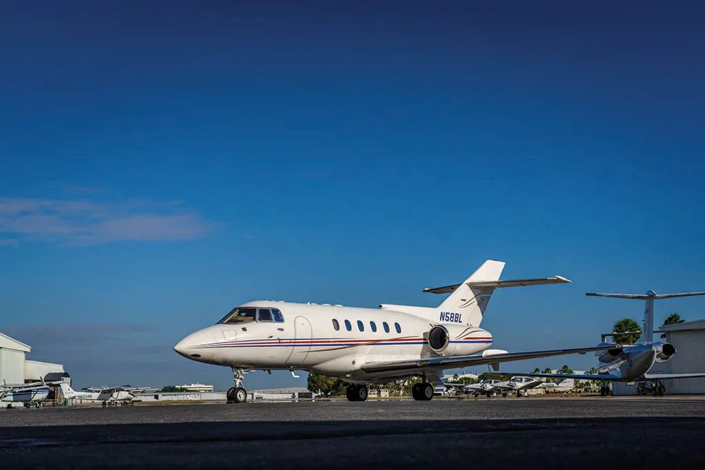 A white Dassault Falcon 50, registration N58BL, with red and blue stripes, parked on an airfield under a clear blue sky.