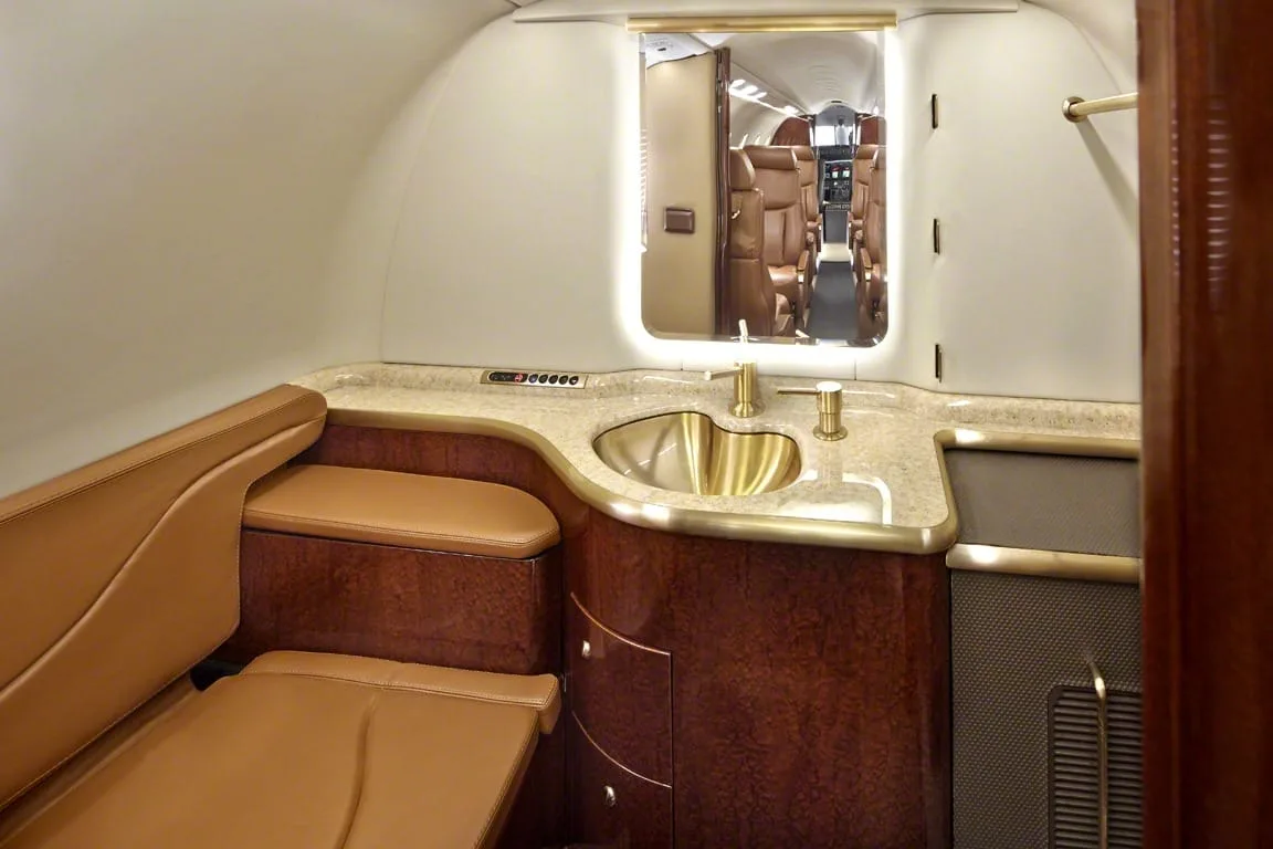 A luxurious aircraft lavatory with a gold sink, marble countertop, and wood cabinetry.