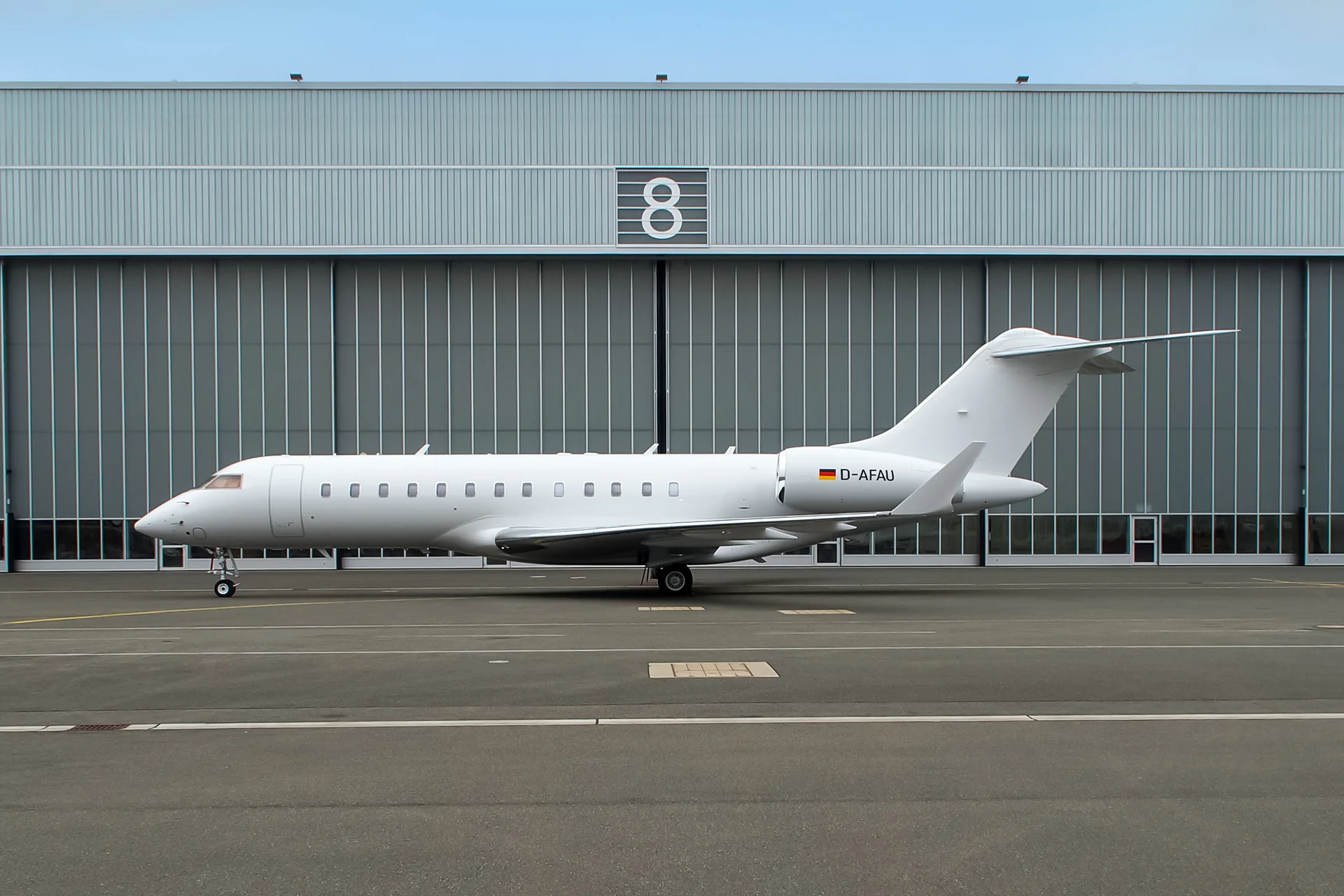 A white Bombardier Global Express business jet with German registration D-AFAU parked in front of a grey hangar.