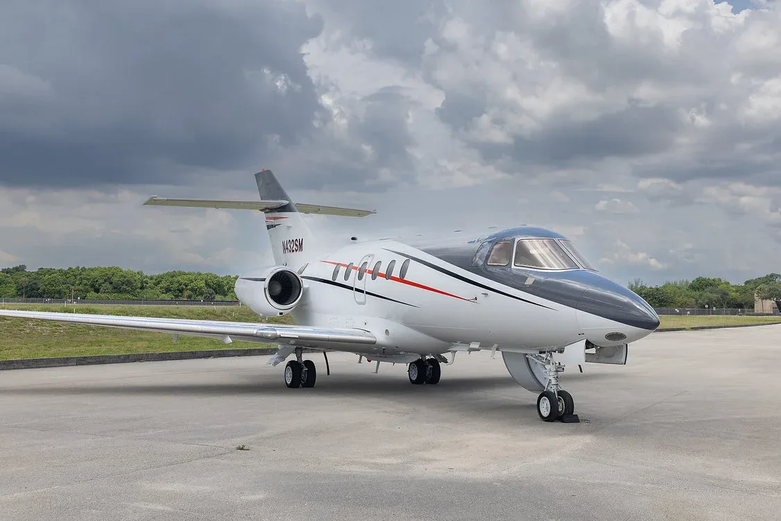 A white and black business jet with red and black stripes, registration N432SM, parked on an airfield under a cloudy sky.