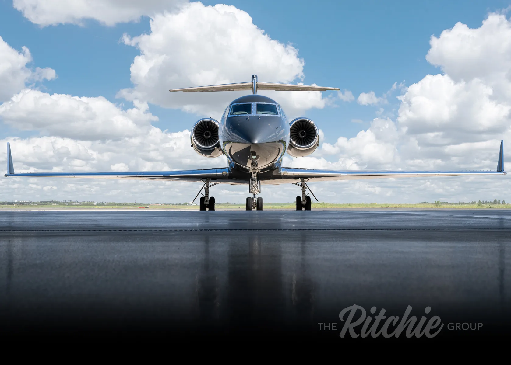 A dark grey Gulfstream G650 business jet parked on a tarmac under a partly cloudy sky, viewed from the front.