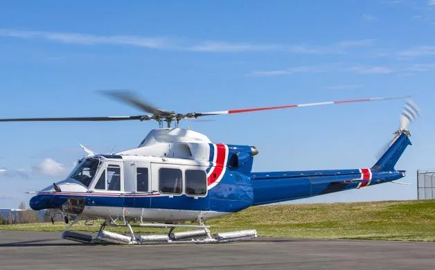 A blue and white helicopter with red accents sits on a tarmac under a clear blue sky, with its rotors slightly blurred.