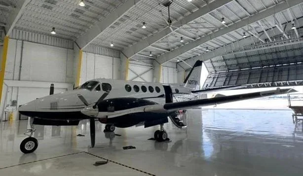 A white and black twin-engine turboprop aircraft, registration N207SB, is parked inside a brightly lit hangar.