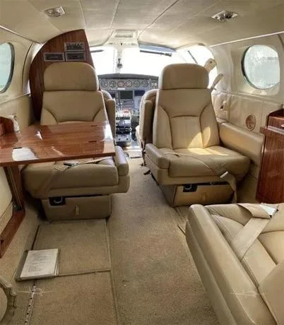 The tan leather interior cabin of a Cessna 414 Chancellor aircraft, showing passenger seats, a fold-out table, and a view towards the cockpit.