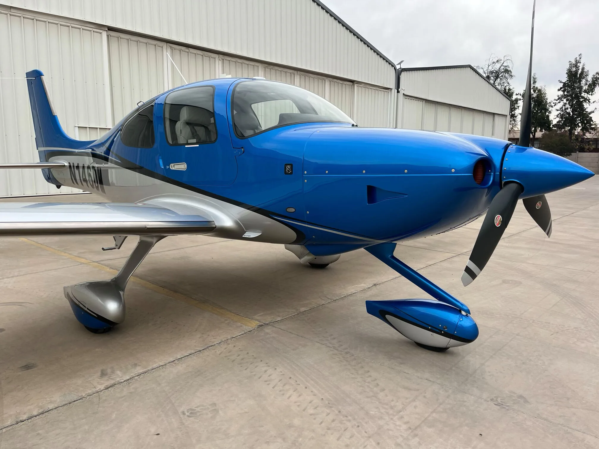 A front three-quarter view of a blue and silver Cirrus SR22 GTS aircraft parked on an apron.