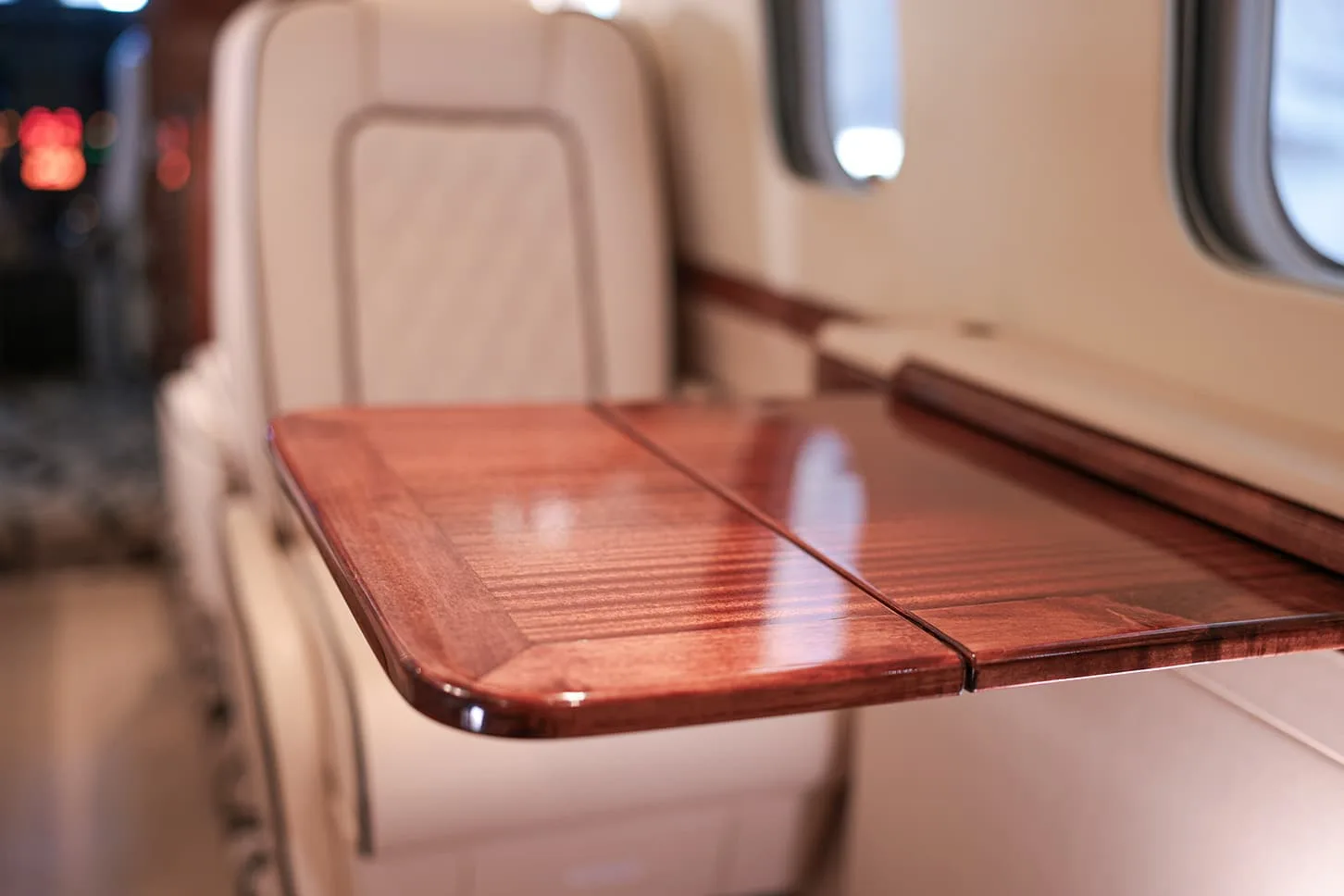 A polished wooden fold-out table in the private jet's cabin, with a cream seat in the background.