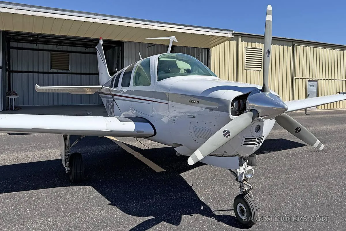 A front-quarter view of a white Beechcraft Baron with maroon and grey stripes, parked on an asphalt ramp.