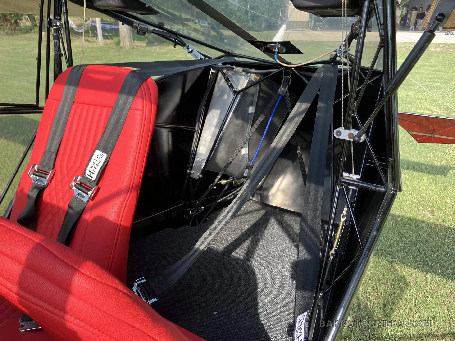 The interior of an aircraft cabin, showing a red seat with a harness and the exposed structural framework.