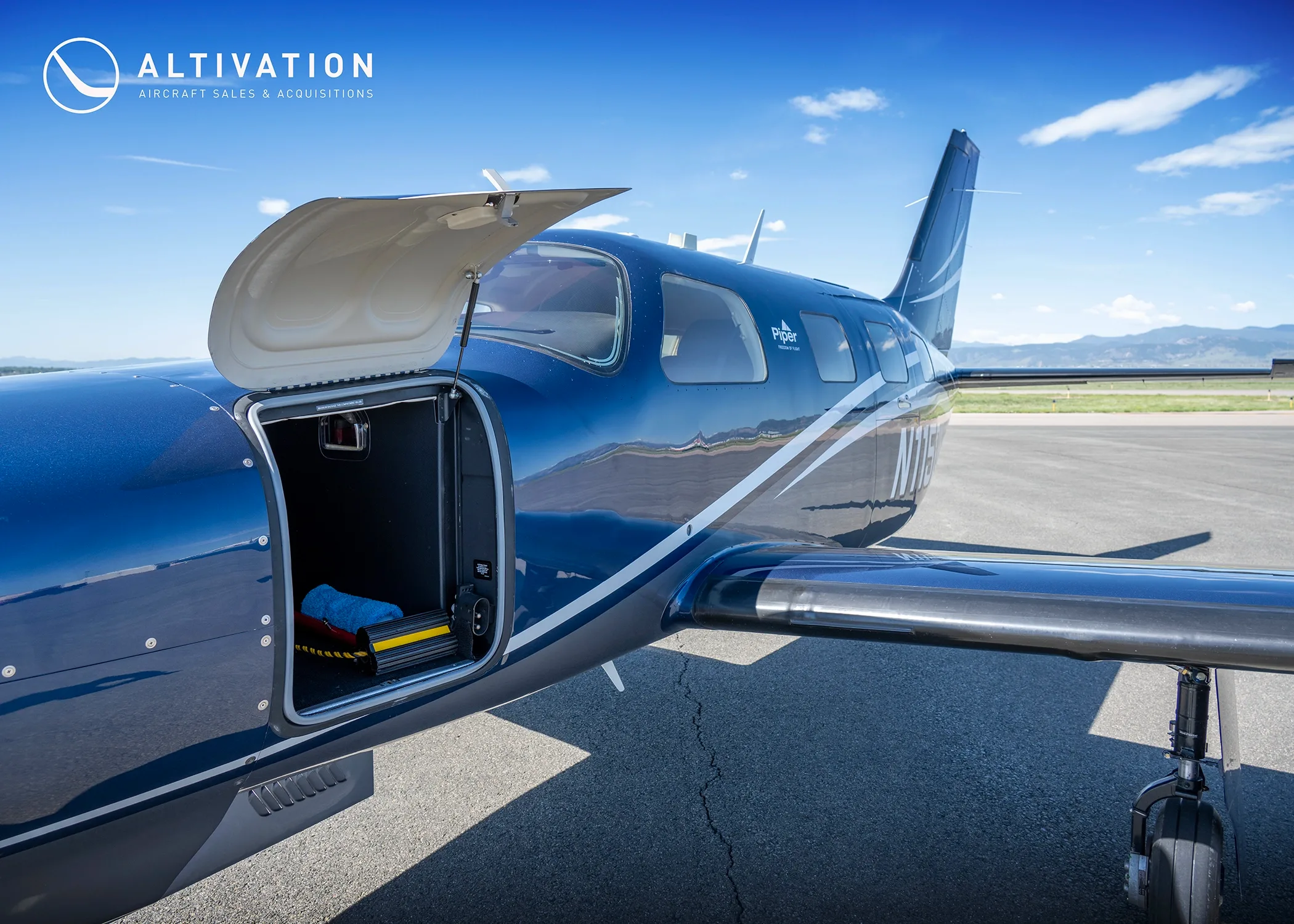 A close-up side view of the dark blue Piper M350, tail number N115DW, with its cargo door open.