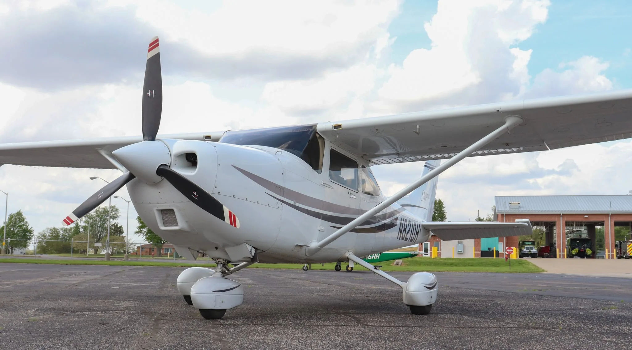 A front-left view of the white Cessna Skylane N821DH with a propeller, parked on an asphalt tarmac.