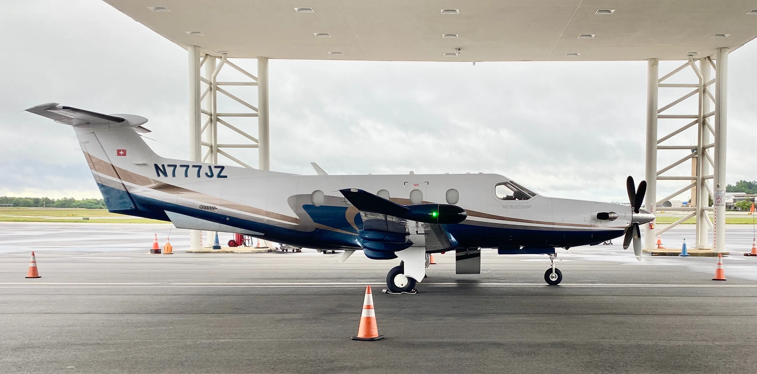 A Pilatus PC-12 aircraft with registration N777JZ is parked under a covered area.
