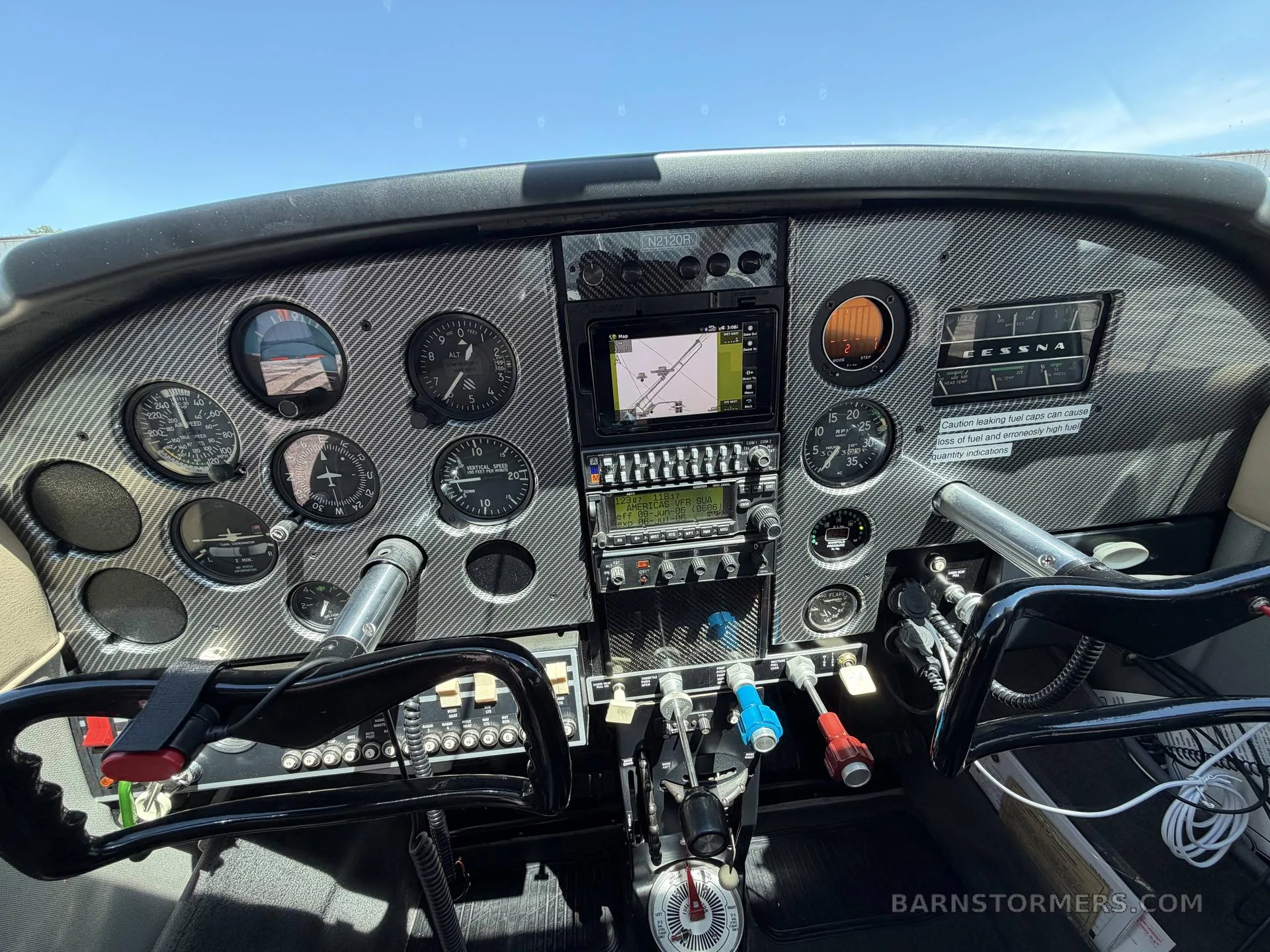 The cockpit of a Cessna aircraft with a carbon fiber-look instrument panel, multiple gauges, and a GPS display.