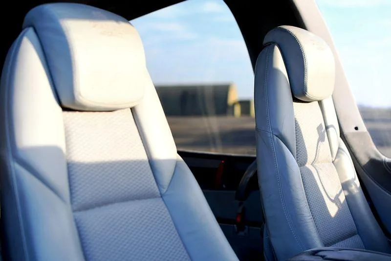 Two light-colored leather aircraft seats with an airfield visible through the window.