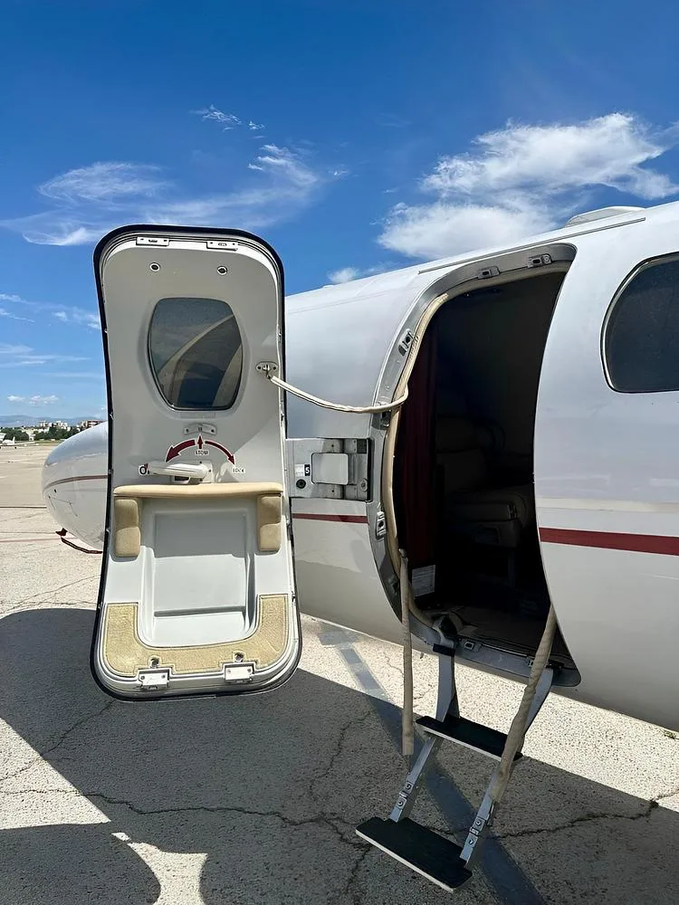 The main entry door of a white Cessna CitationJet aircraft is open with stairs extended, revealing a glimpse of the interior.