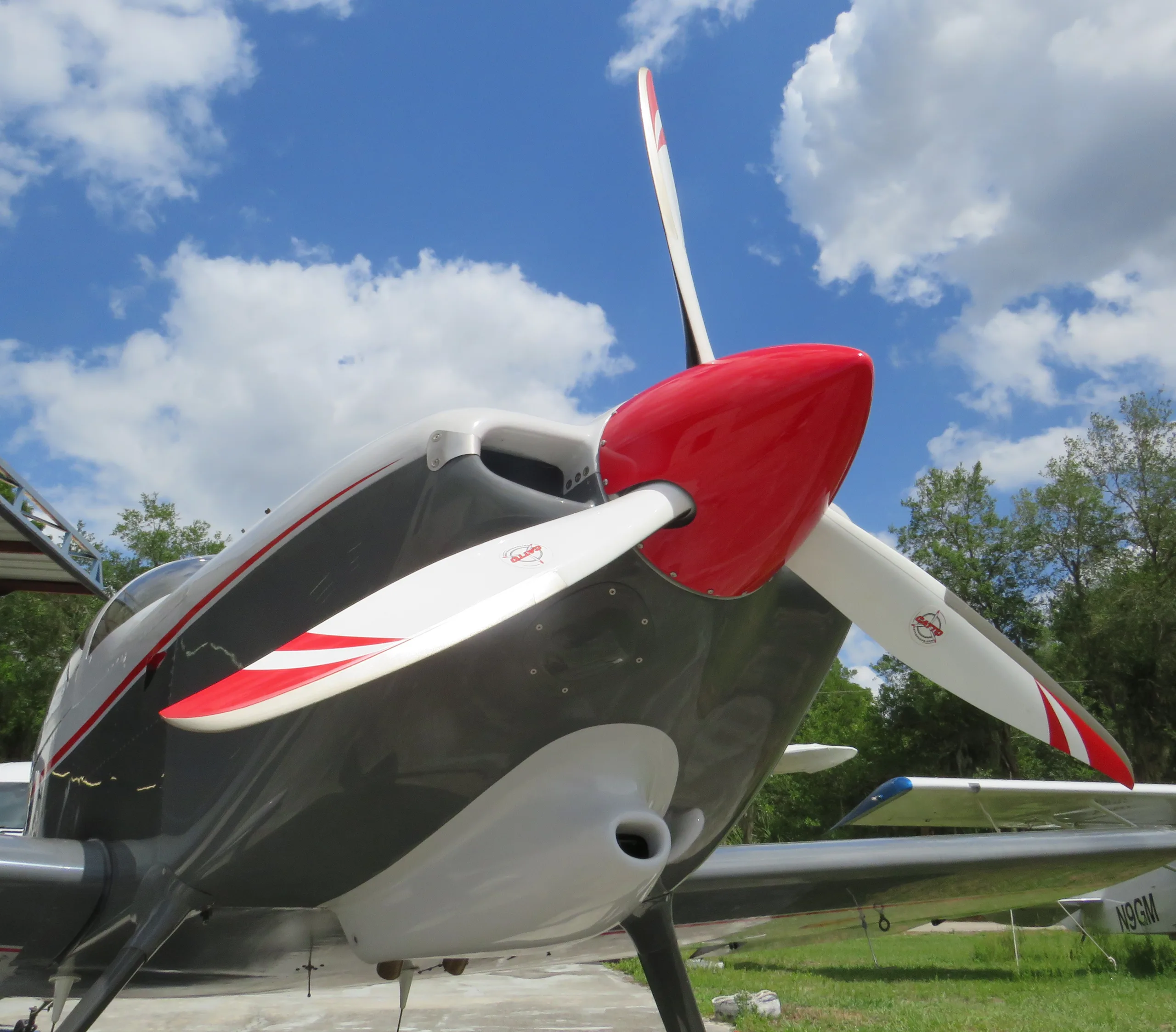 A close-up view of the nose and propeller of a grey and white aircraft with red accents, under a blue sky.