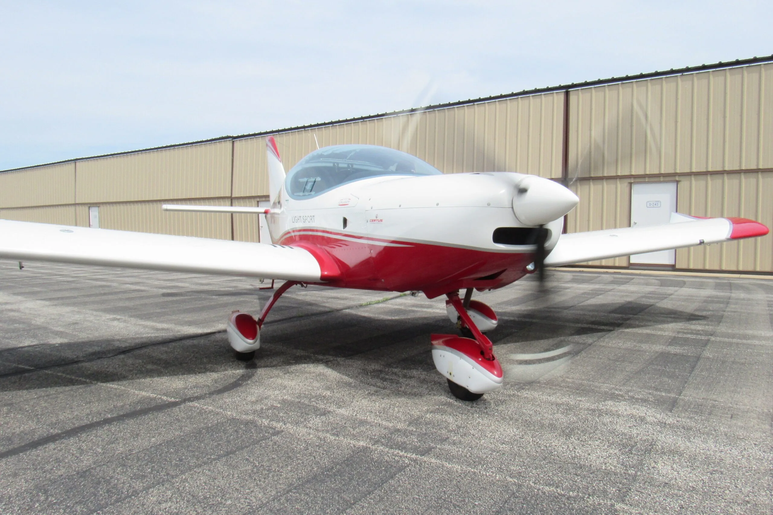 A white and red SportCruiser aircraft with a spinning propeller on an airport tarmac.