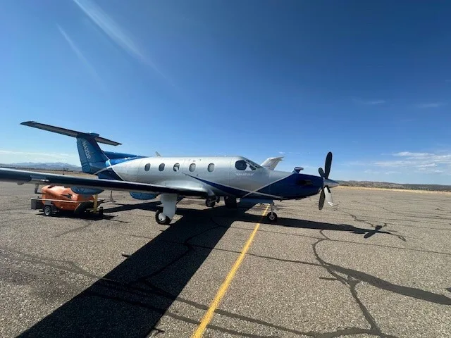 A Pilatus PC-12 aircraft with registration N42DP parked on an airfield under a clear blue sky with mountains in the distance.