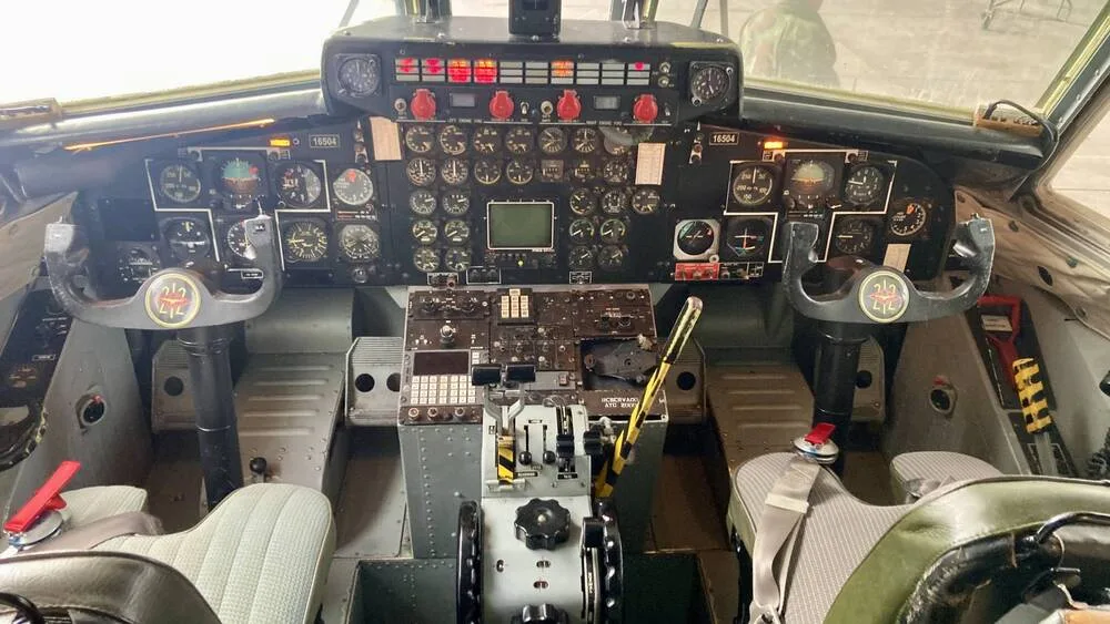 The detailed cockpit of a military transport aircraft with numerous analog gauges and controls.