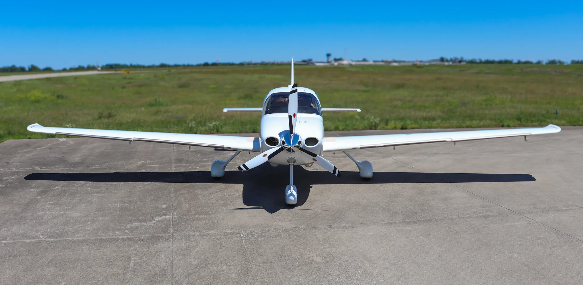 Head-on view of a white Cirrus SR22 aircraft with a three-bladed propeller on a tarmac.