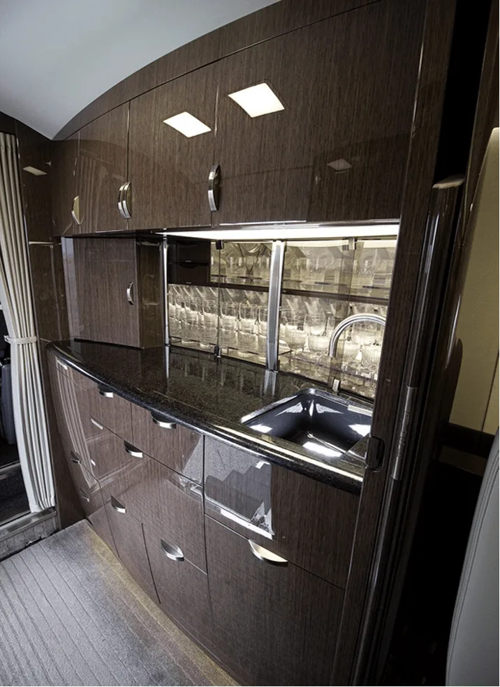 A luxurious aircraft galley with dark wood cabinetry, a black countertop, a sink, and glassware storage.