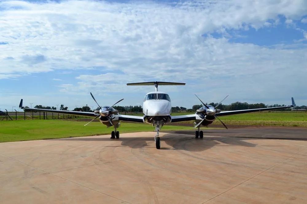 A head-on view of a white and blue Beechcraft King Air twin-turboprop aircraft with its propellers visible, parked on a tarmac.