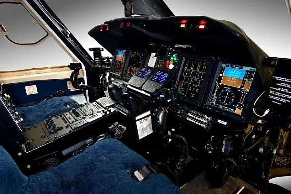The modern cockpit features multiple digital displays, control panels, and a blue-covered pilot's seat.