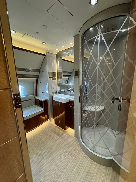 A luxurious aircraft lavatory features a modern sink, mirrors, and a glass-enclosed shower with a geometric pattern.