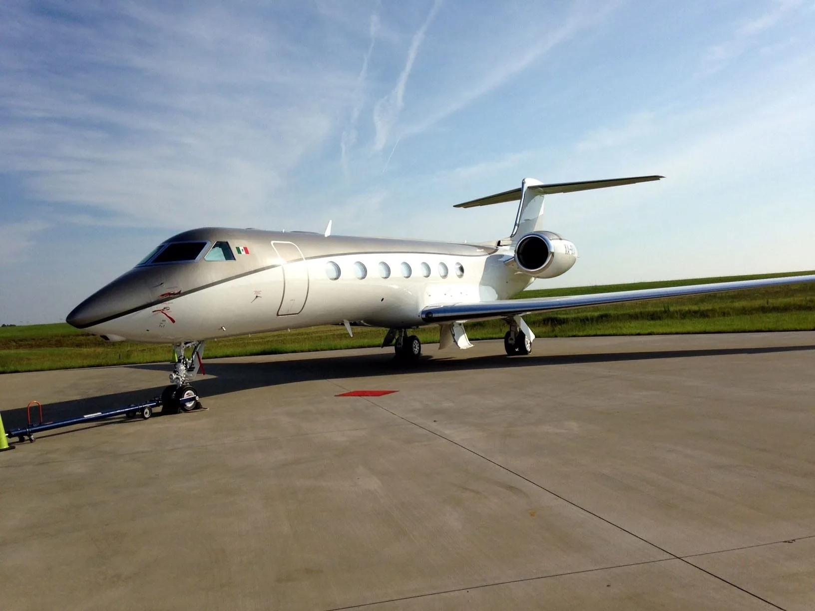 A Gulfstream G550 business jet with a silver and dark grey paint scheme parked on an airfield under a blue sky.