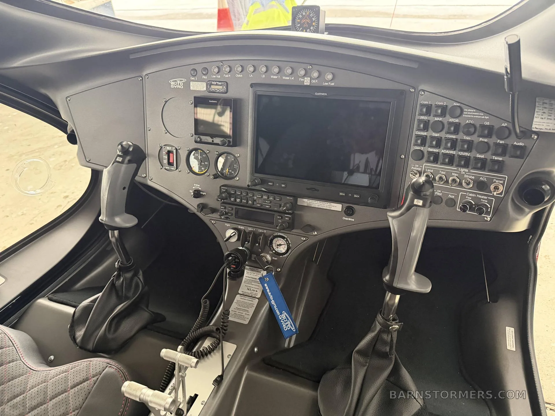 The cockpit of an AutoGyro Cavalon 915iS, showing the instrument panel with two large Garmin displays and dual controls.