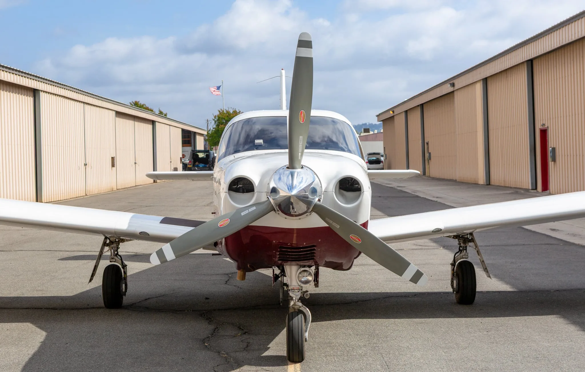 Front view of a white and maroon Piper Saratoga II TC aircraft, registration N691MA, parked between hangars.