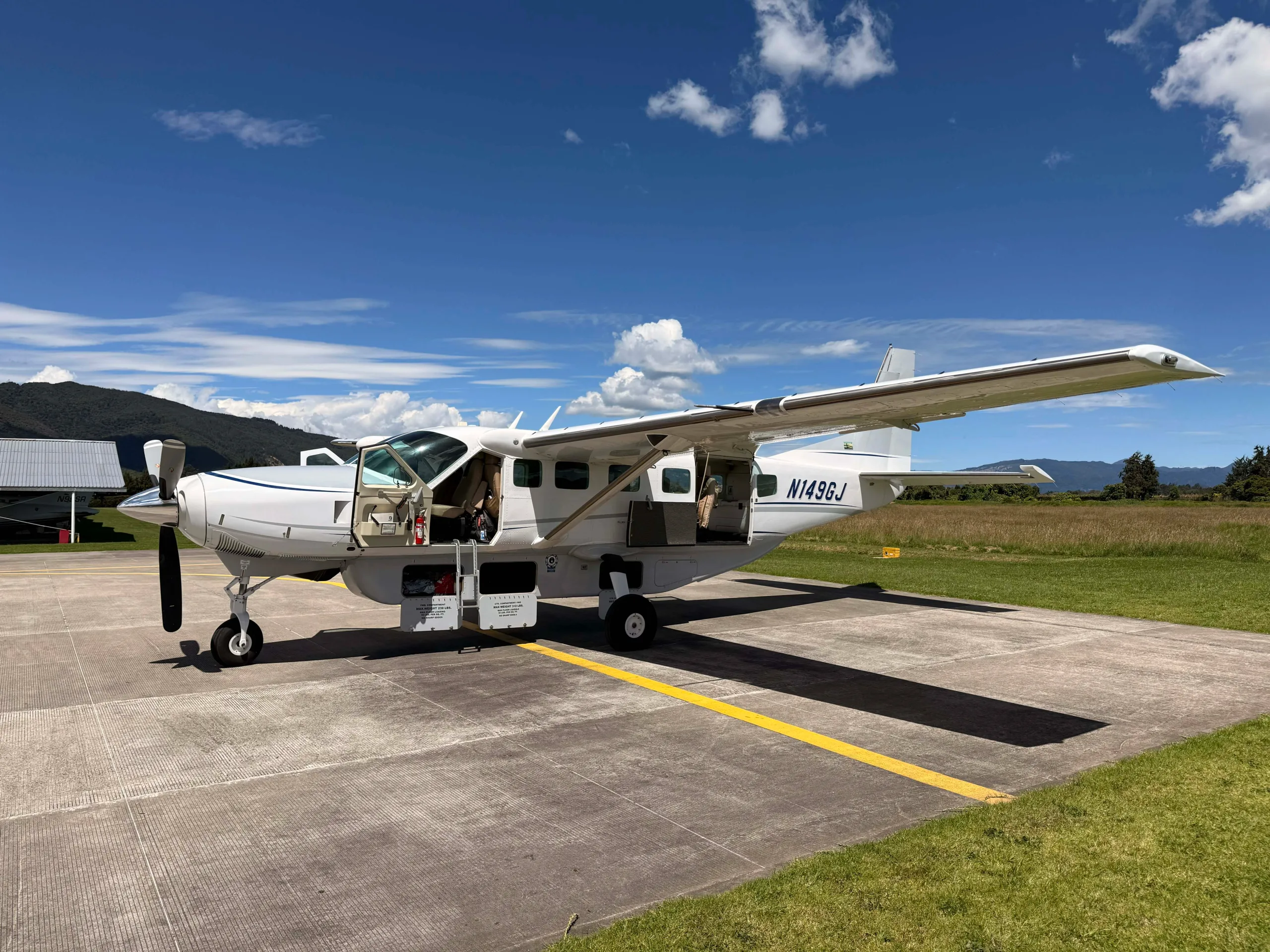 A white Cessna Caravan N149GJ with open doors parked on an airfield under a blue sky.