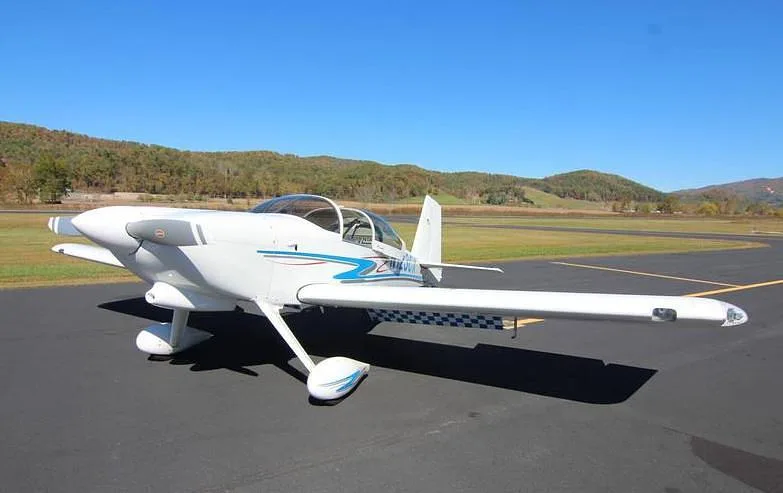 A white N123CX aircraft with blue and gray stripes parked on an asphalt runway on a sunny day with distant mountains.