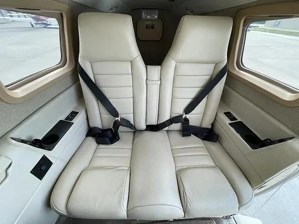 The light beige leather passenger seats in the aircraft cabin are visible, with windows on either side.