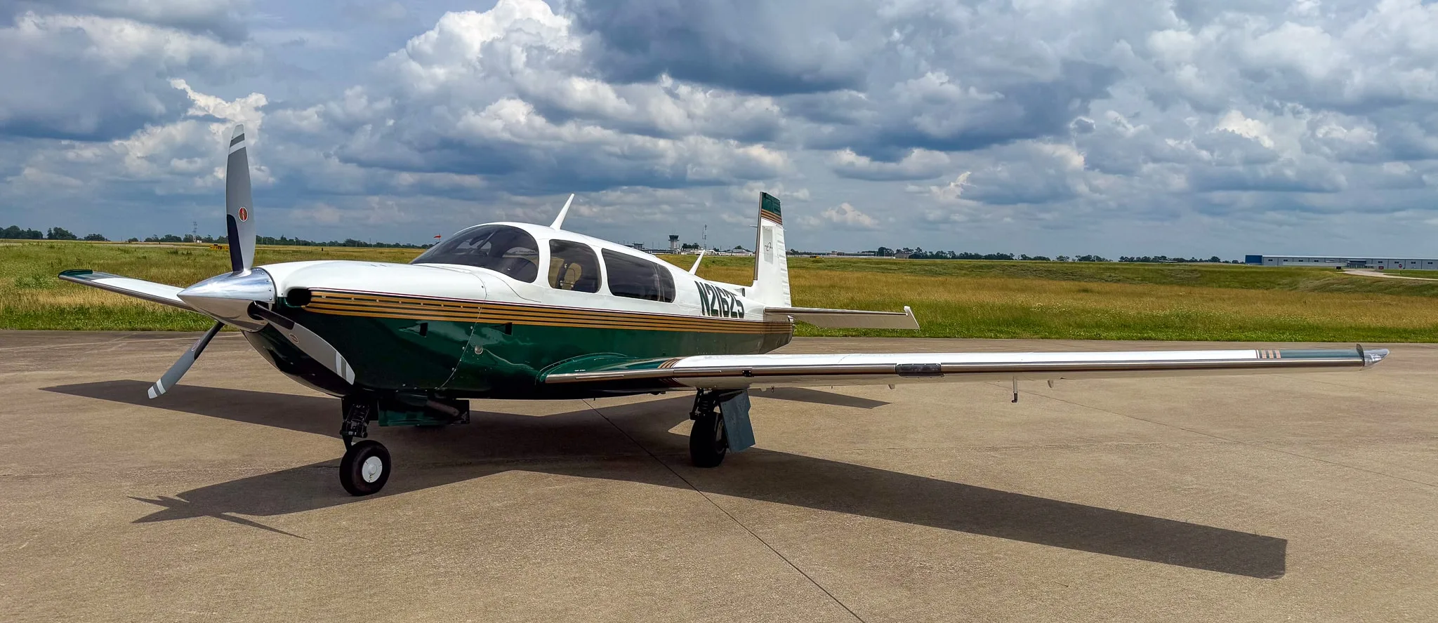 A white and green Mooney M20 aircraft with registration N21625 parked on an airfield under a cloudy sky.