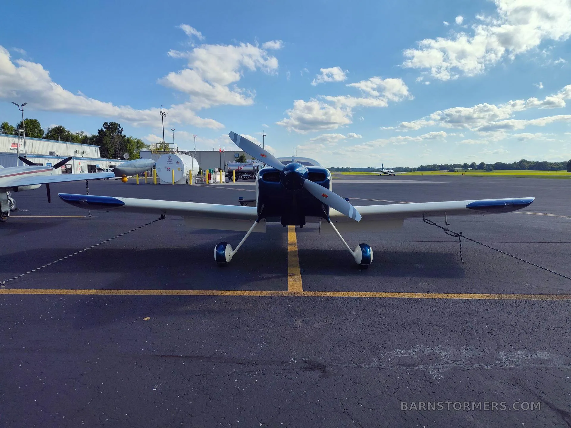A cream and blue single-engine aircraft with red and grey stripes, viewed head-on, parked on an asphalt tarmac.