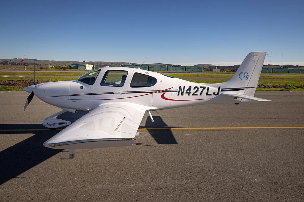 A white single-engine aircraft, N427LJ, with red and black stripes, parked on an asphalt runway under a clear blue sky.