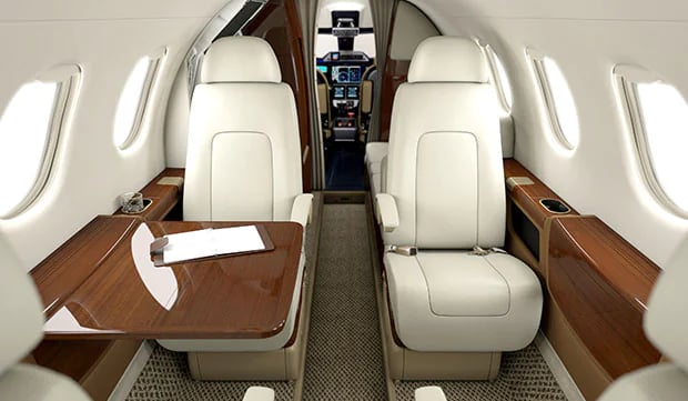 A view of the aircraft's interior with white leather seats and a wooden table.