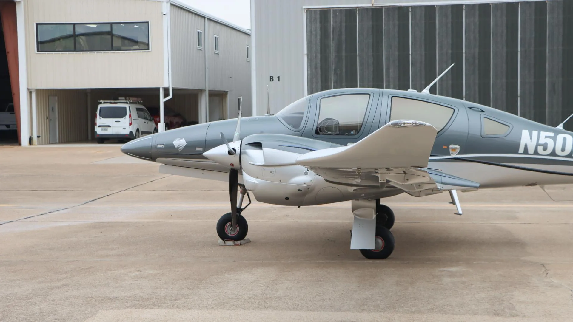A close-up side view of the front section of the gray and silver Diamond DA62 aircraft, N502LA, on the tarmac.