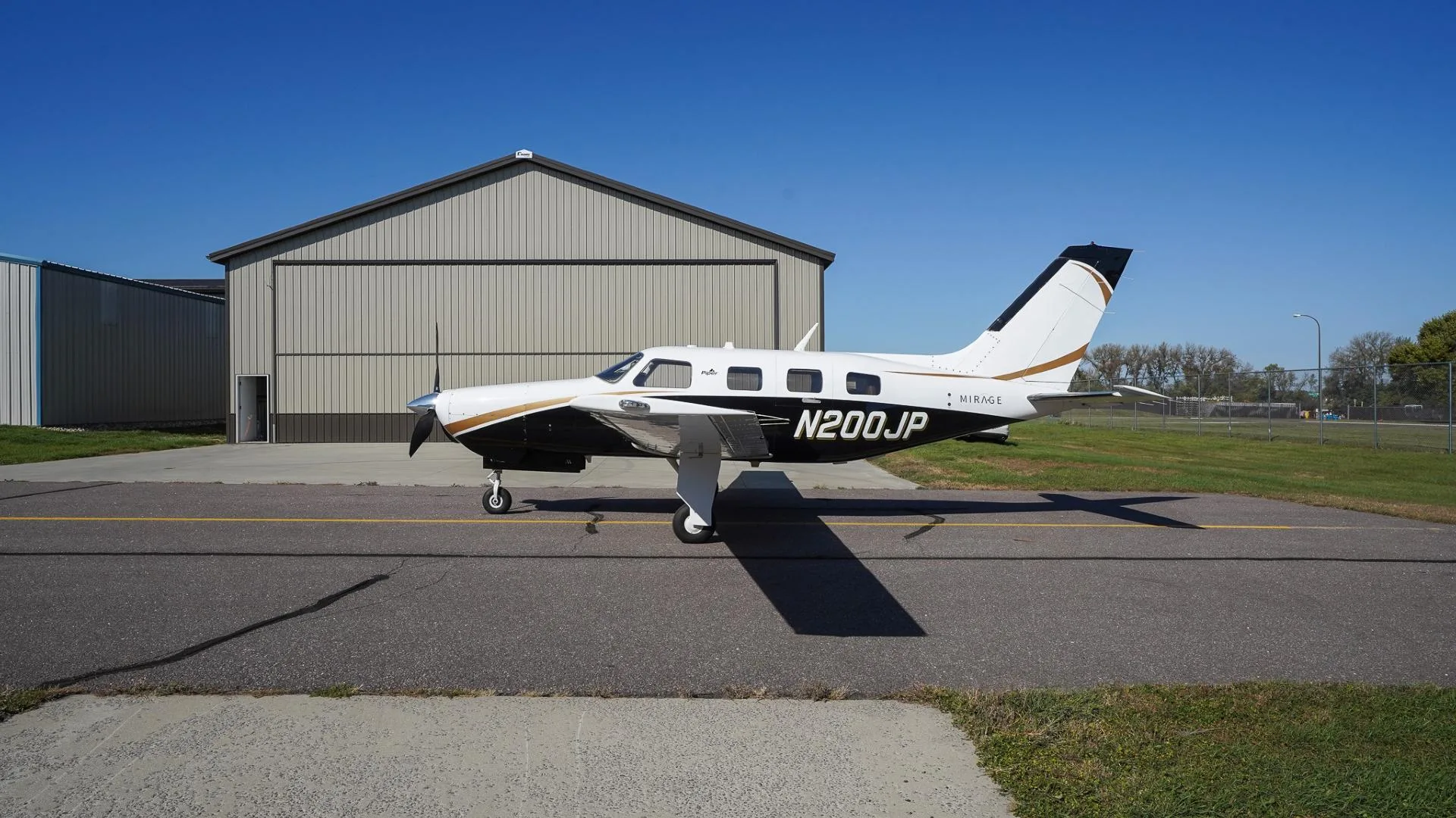 A side view of a white and black Piper Mirage N200JP with gold accents parked on an airfield.