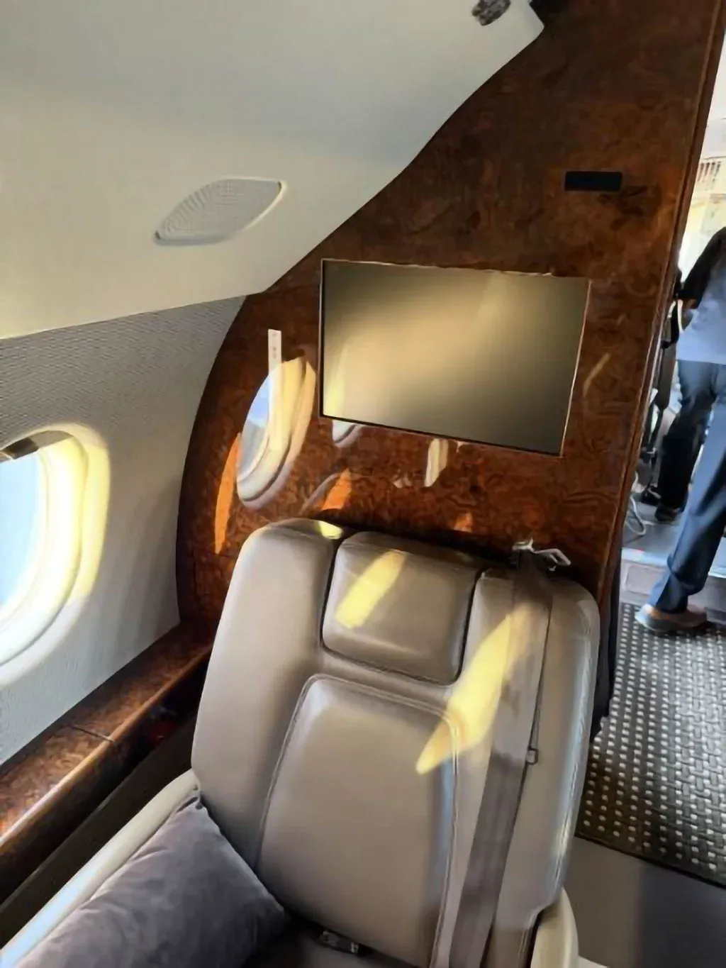 A brown leather cabin seat with a monitor mounted on a wood-paneled wall, next to an aircraft window.