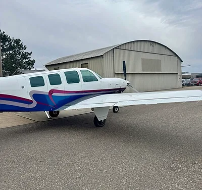 Side view of a Mooney aircraft parked on the tarmac, showing the wing and fuselage.