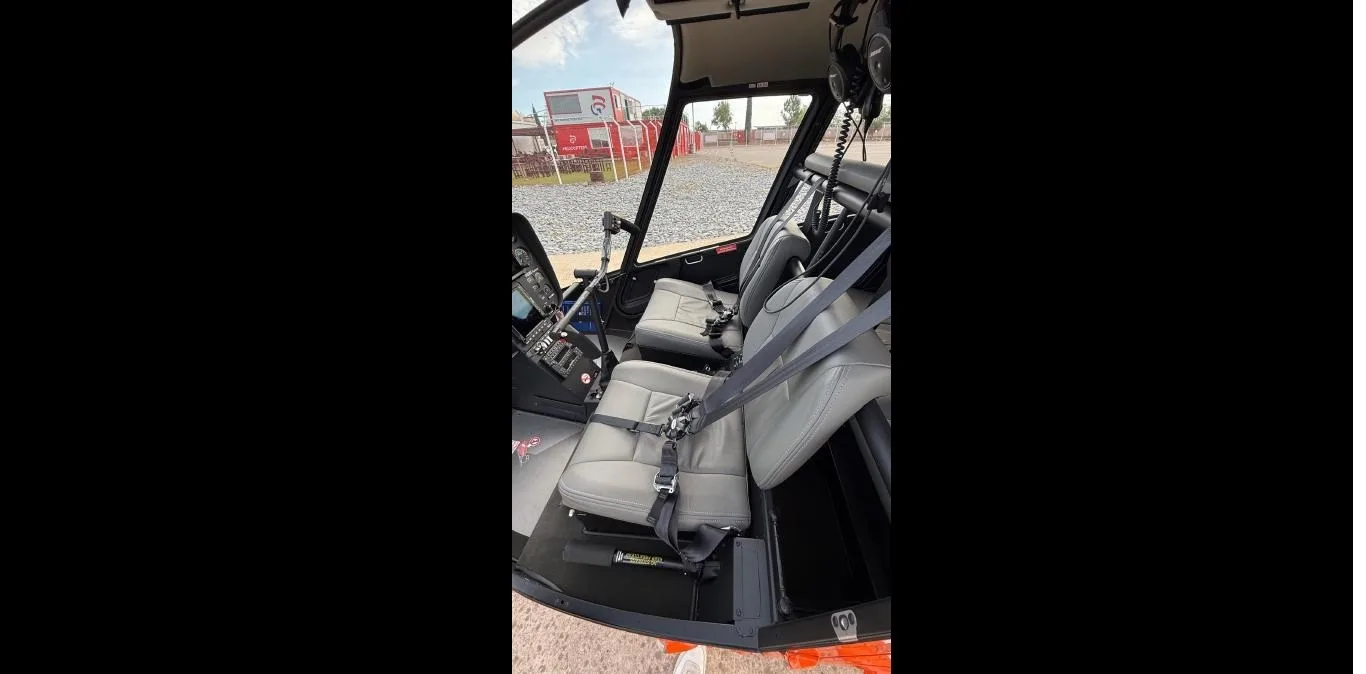 The gray front and rear cabin seats of an orange Robinson R66 helicopter, with some cockpit controls visible.